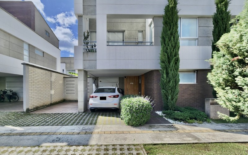 This stunning white house features two parking spaces (one covered and one uncovered) and a charming front garden with a pine tree. Perfect for those looking for a serene and inviting home in a gated community.